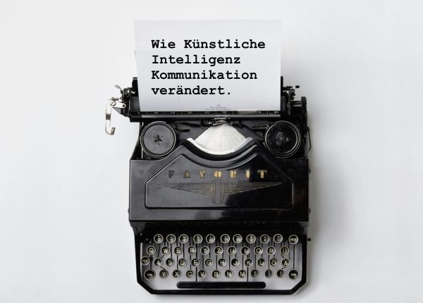 Schreibmaschine mit weissem Blatt Papier und Text "Wie Künstliche Intelligenz Kommunikation verändert"