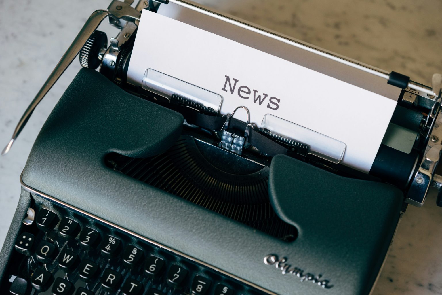 Schreibmaschine mit weissem Blatt Papier, auf dem NEWS steht.